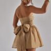 Woman in a gold strapless SEQUIN BOW CORSET DRESS with a large sequin bow on the back poses looking over her shoulder.