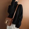 Woman in a black LOOSE CASHMERE SWEATER with a brown shoulder bag.