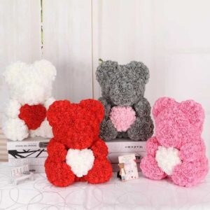 Four Teddy Bears of Roses in white, red, gray, and pink are displayed on books and a table. Each Teddy Bear of Roses has a heart shape on its chest.