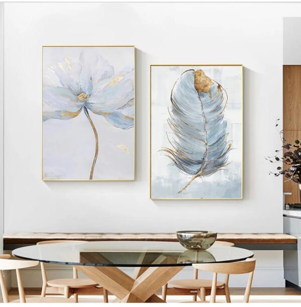 Two framed artistic prints on a wall, one depicting an abstract SCANDINAVIAN FLOWER and the other a feather, above a modern dining table with chairs.