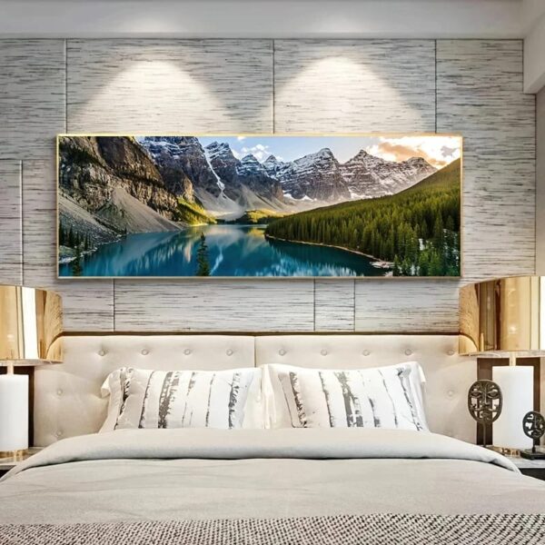 A modern bedroom features a large Landscape Wall Art of a mountainous lake above a neatly made bed with patterned pillows. The room has a neutral color scheme and metallic bedside lamps.