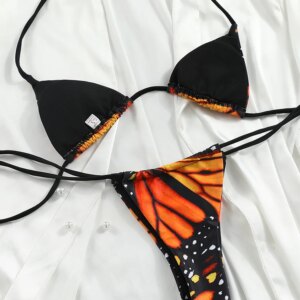A BUTTERFLY GIRL TWO PIECE SWIMSUIT featuring a black and orange butterfly pattern lies flat on a white fabric background.