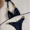 A black TWO PIECE BRAZILIAN BIKINI SET with gold chain accents on the straps is displayed on a light fabric background.