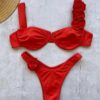 A red FLOWER DIVA TWO PIECE SWIMSUIT with rose embellishments on one shoulder strap and one side of the bottoms, laid out on a light-colored surface next to a straw hat.