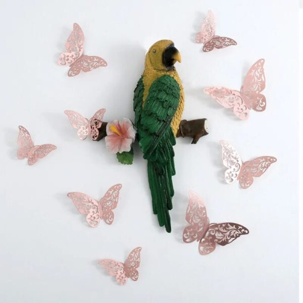 A decorative parrot sculpture with green and yellow feathers is mounted on a white wall, surrounded by 12Pcs Fashion 3D Hollow Butterfly ornaments in a delicate pink lace-like design.