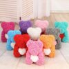 A collection of Teddy Bears of Roses, crafted from vibrant artificial flowers, arranged in two rows on a wooden floor against a white folding screen.