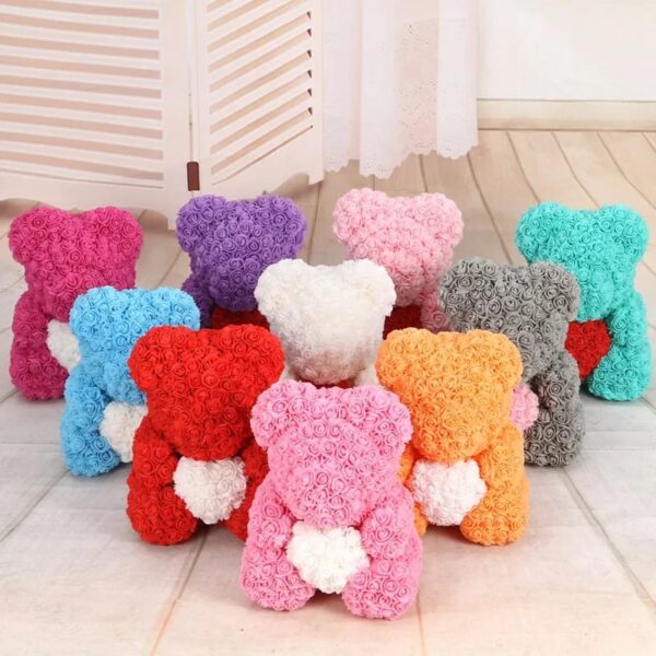 A collection of Teddy Bears of Roses, crafted from vibrant artificial flowers, arranged in two rows on a wooden floor against a white folding screen.