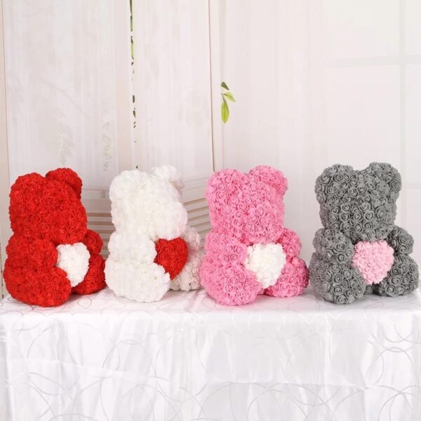 Four Teddy Bear of Roses in red, white, pink, and gray, each adorned with a heart on the front, are displayed on a white textured tablecloth.