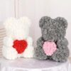 Two Teddy Bears of Roses sit on a table; one white bear holds a red heart, and one gray bear holds a pink heart.